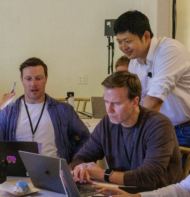 Kevin Bai helping two attendees at their laptops during the build hour